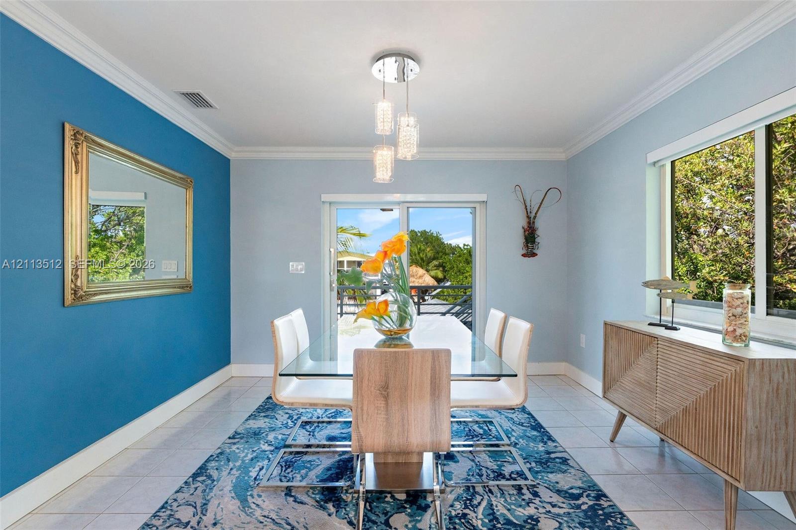 Dining area featuring crown molding, a modern three-light glass pendant fixture, sliding glass doors, and light-toned tile flooring