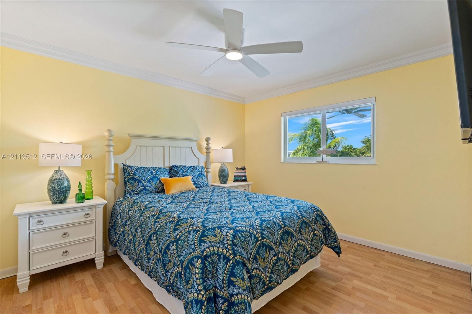 Room featuring wood-finish flooring, crown molding, a central ceiling fan with integrated lighting, and a window with exterior greenery