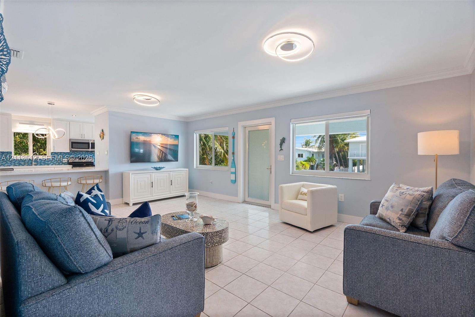 Open-concept interior featuring light-colored tile flooring, contemporary circular LED flush-mount lighting, and large windows with horizontal panes