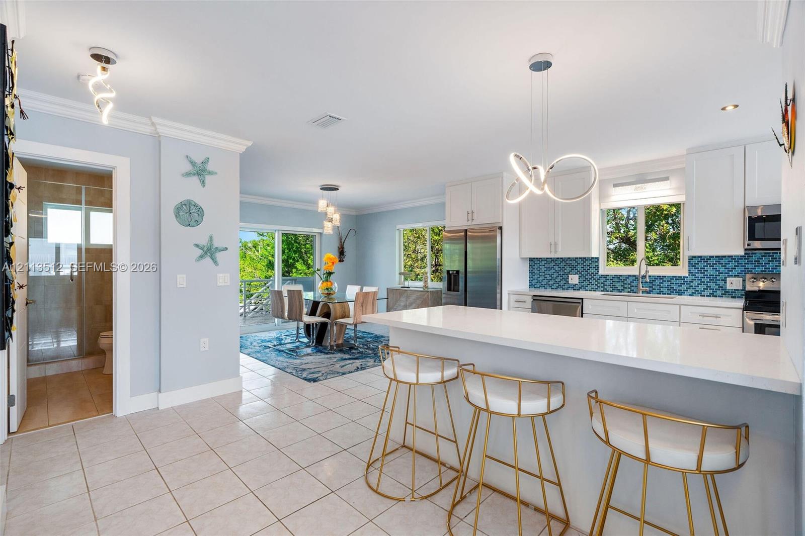 Kitchen featuring a white quartz countertop island, white cabinetry, blue geometric tile backsplash, and stainless steel appliances