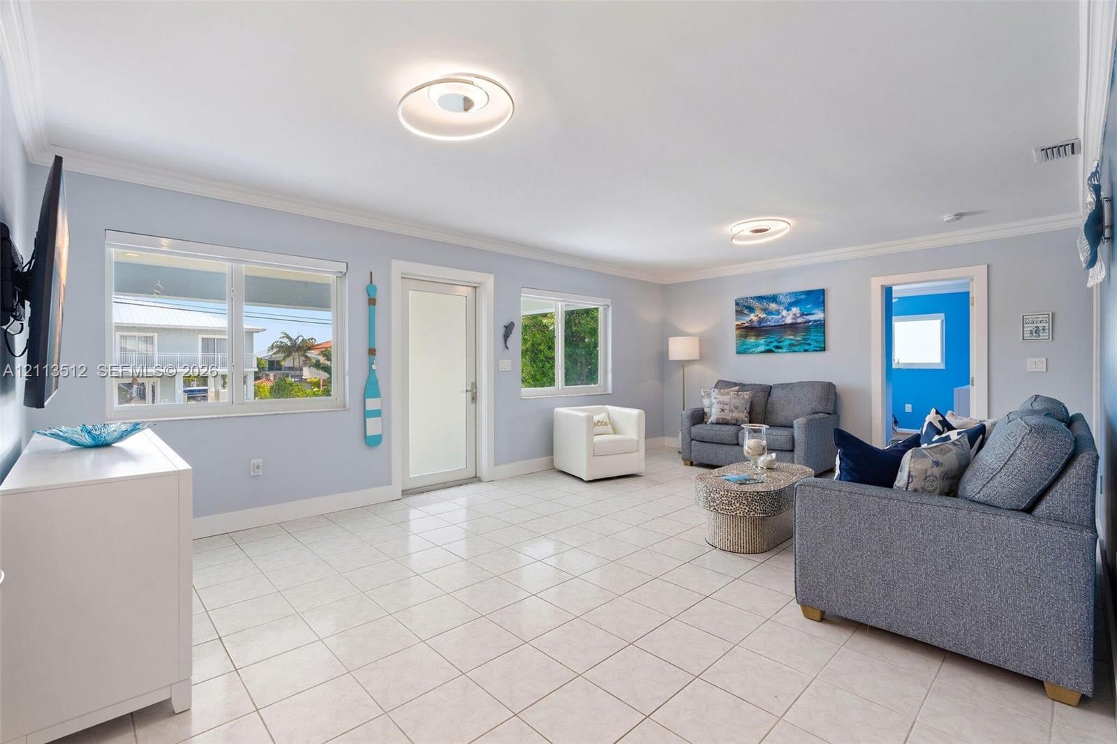 Open-concept room featuring light-toned tile flooring, recessed crown molding, and circular modern flush-mount lighting fixtures