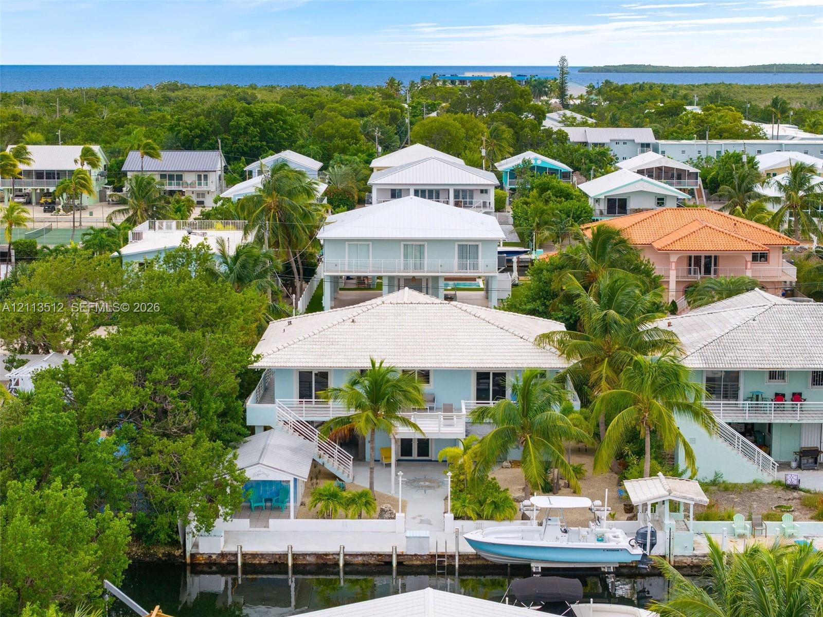 Waterfront residence featuring a private boat dock, elevated deck, light-toned exterior finish, and mature palm trees