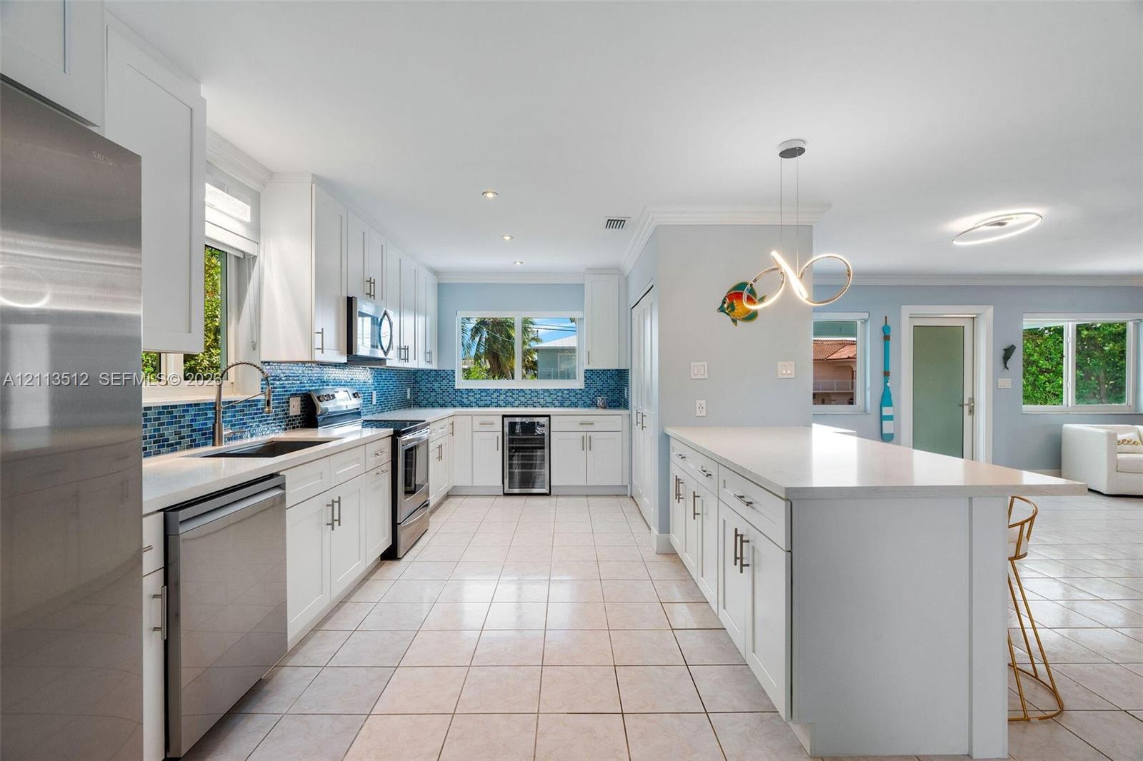 Kitchen featuring white shaker-style cabinetry, quartz countertops, a blue glass tile backsplash, stainless steel appliances, and a built-in beverage refrigerator