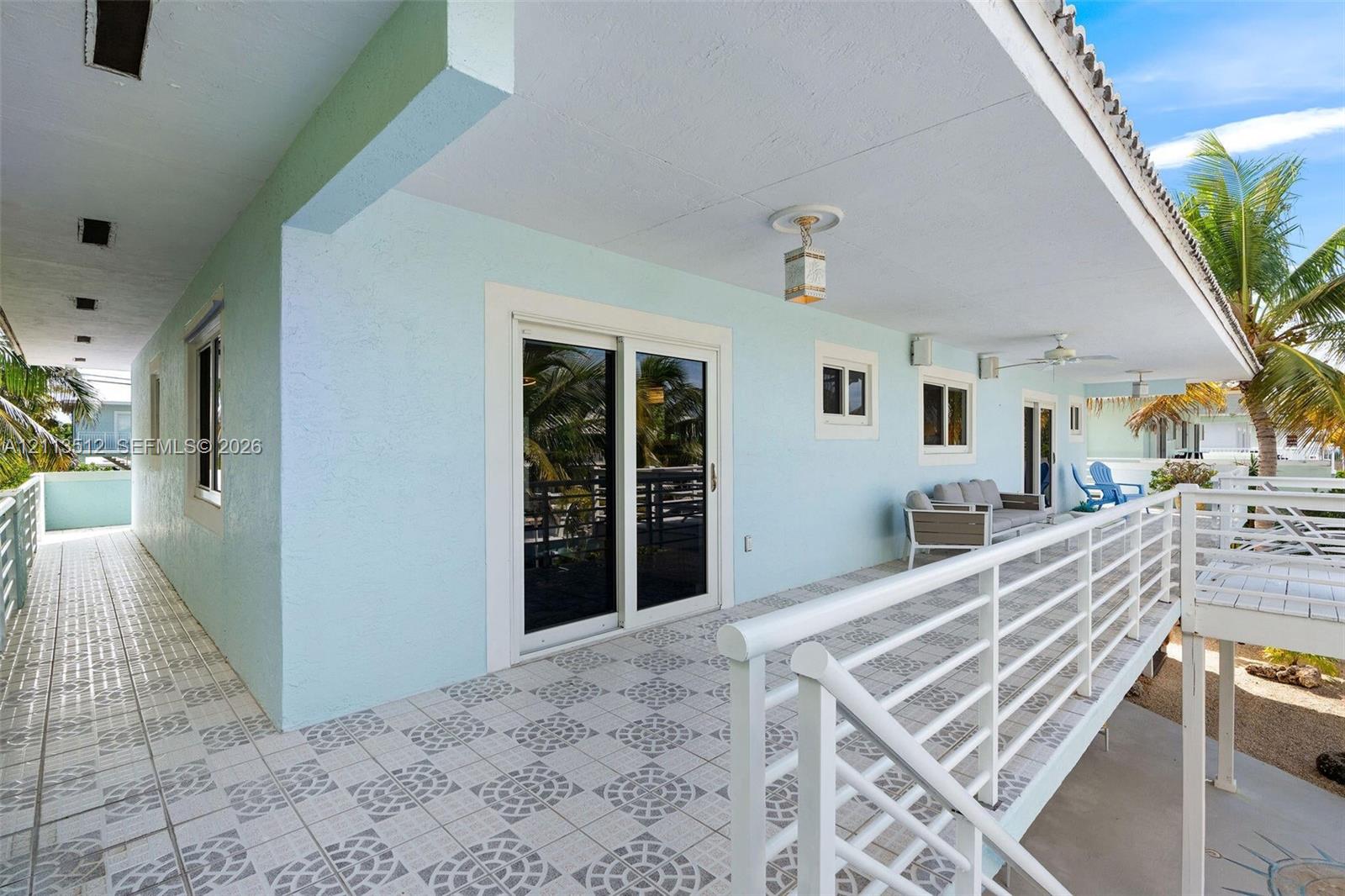 Covered exterior balcony featuring patterned tile flooring, a white metal railing, recessed ceiling lighting, and glass sliding door access