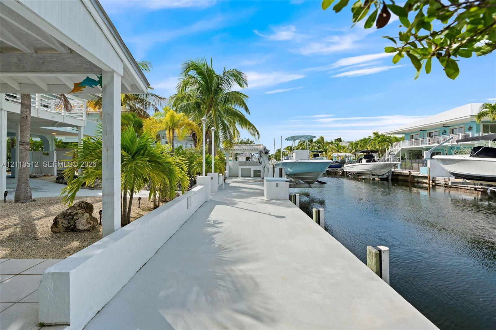 Concrete waterfront bulkhead featuring a paved walking path, integrated light fixtures, and a direct-access boat lift