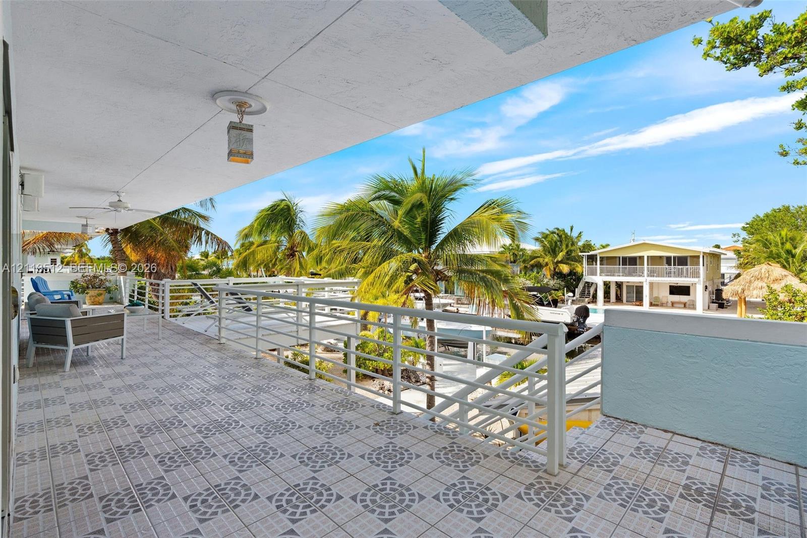 Covered balcony featuring patterned ceramic tile flooring, horizontal metal railings, and dual ceiling-mounted light fixtures