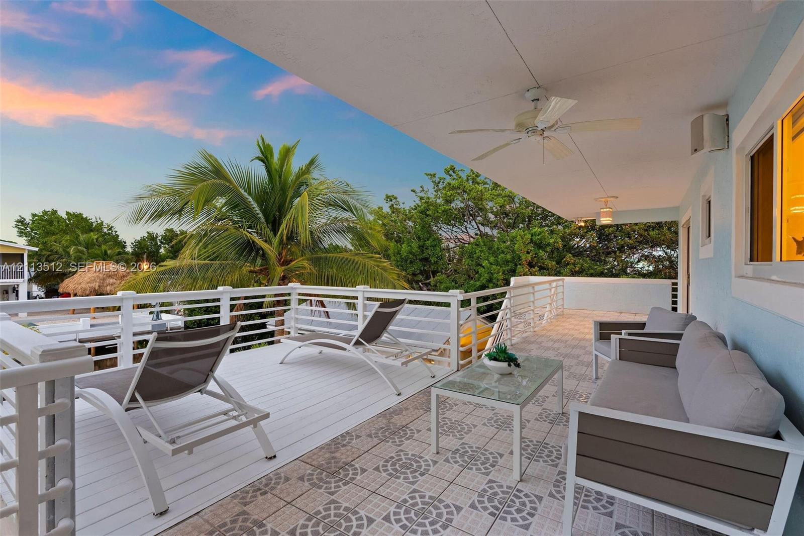 Covered balcony featuring patterned tile flooring, white horizontal railing, and integrated ceiling fans