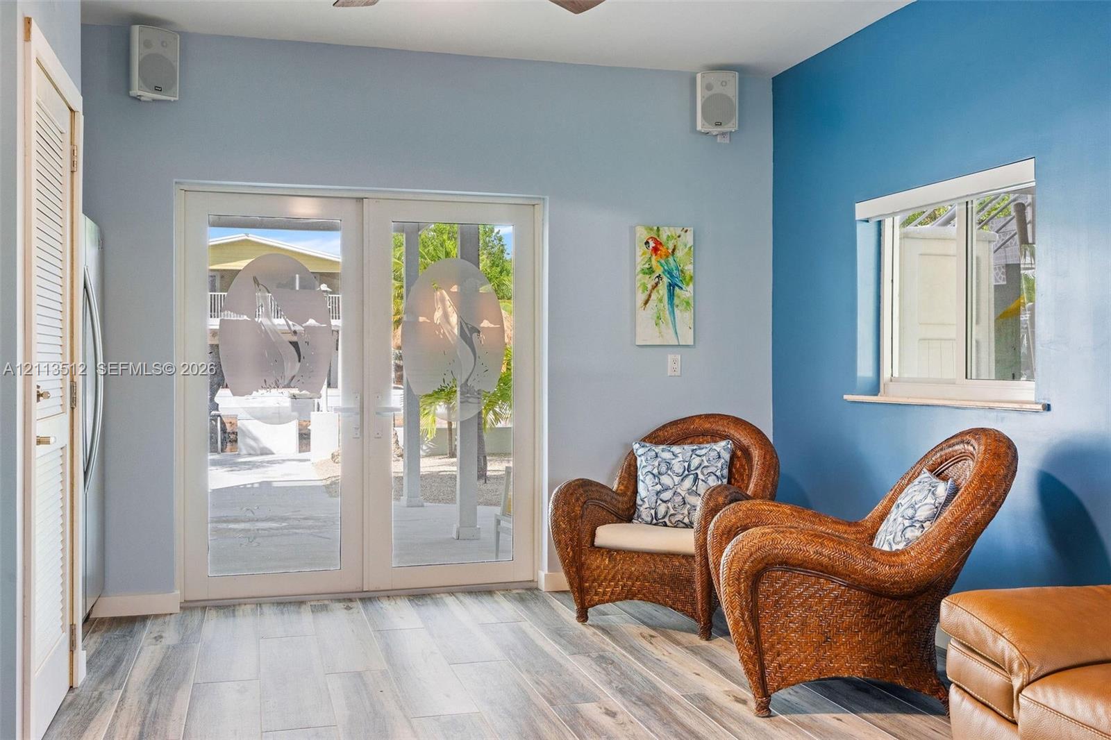 Double French doors featuring frosted glass panels with etched tropical motifs, wood-finish flooring, two wall-mounted speakers, and a louvered closet door