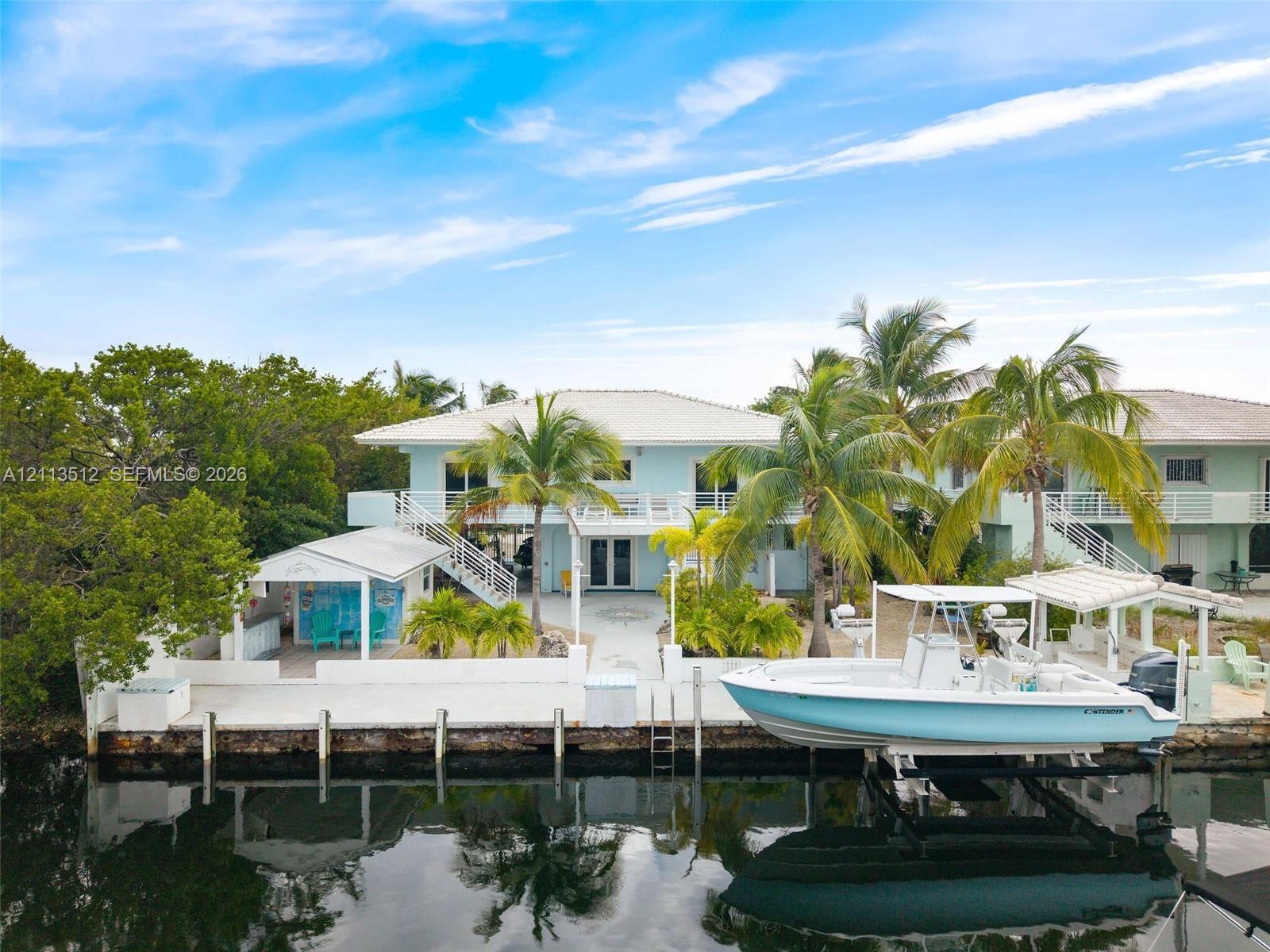 Waterfront property featuring a private boat lift, concrete bulkhead, covered outdoor bar area, and elevated rear deck with staircase access