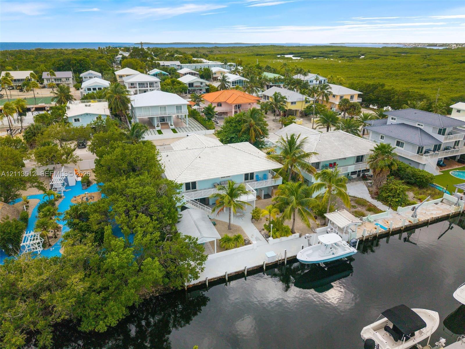 Waterfront property featuring a private boat dock, concrete seawall, tiered tropical landscaping, and mature palm trees