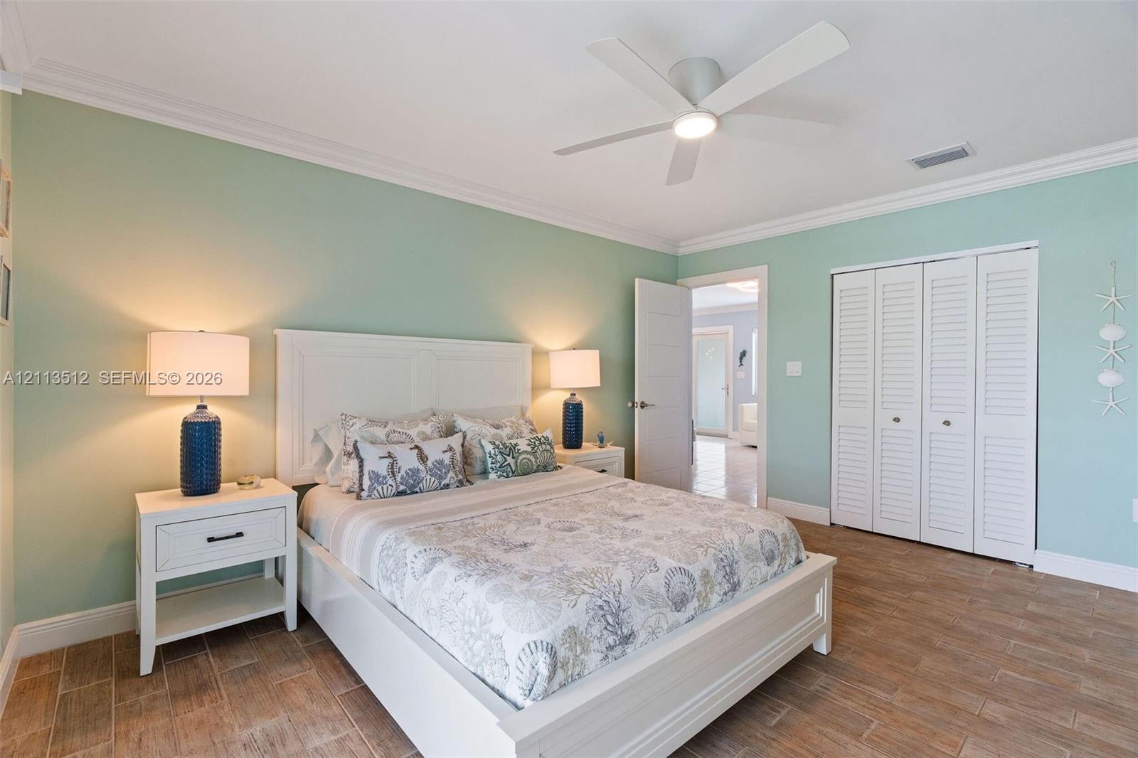 Wood-finish tile flooring, ceiling-mounted light fixture with fan, and closet with white louvered doors