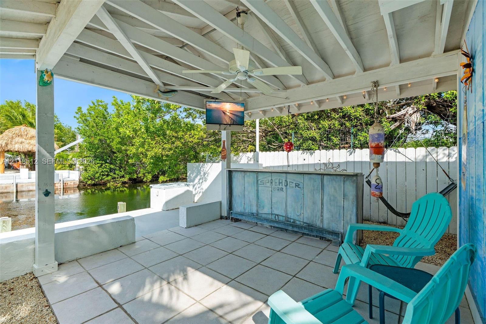 Covered outdoor patio featuring tile flooring, a built-in bar, a ceiling fan, and direct water frontage