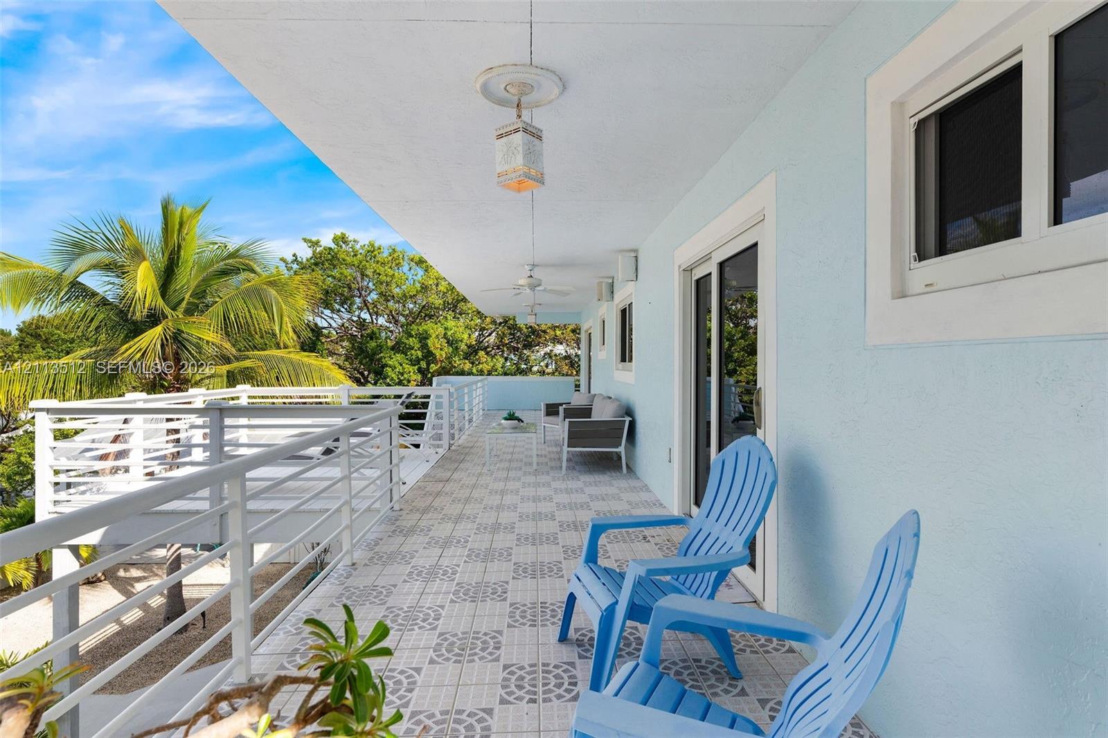 Covered exterior balcony featuring patterned tile flooring, white horizontal-rail fencing, and mounted light fixtures