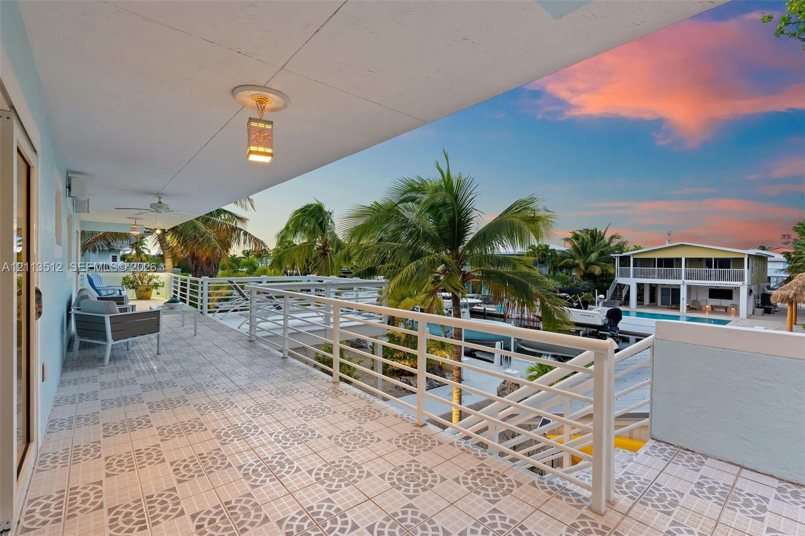 Covered exterior balcony featuring patterned tile flooring, white metal railing, and ceiling-mounted lighting