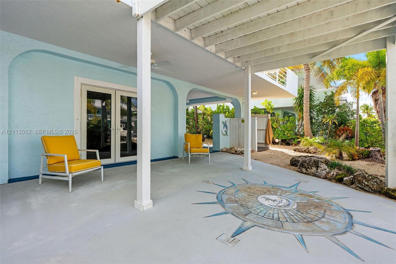 Covered patio featuring a concrete floor with a decorative compass inlay, arched structural supports, French doors, and an outdoor shower area