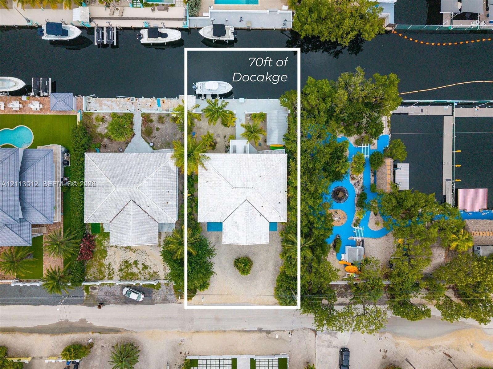 Aerial perspective of a waterfront property featuring 70 feet of canal frontage, a private boat dock, and mature palms