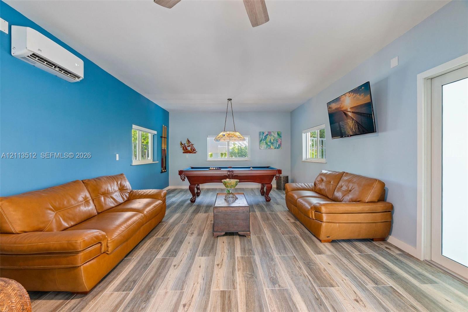 Wood-finish flooring, wall-mounted ductless air conditioning unit, ceiling-mounted light fixture, and multiple windows