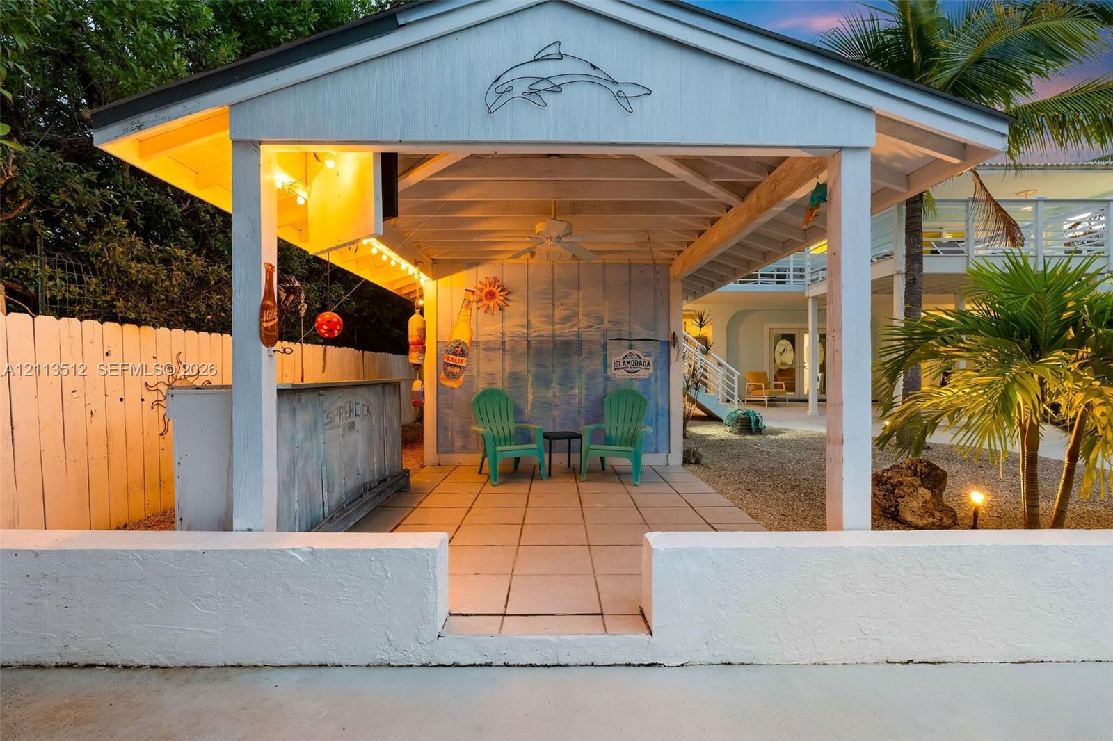 Covered outdoor pavilion featuring a built-in bar, tiled flooring, exposed beam ceiling with a mounted ceiling fan, and a low-profile perimeter masonry wall