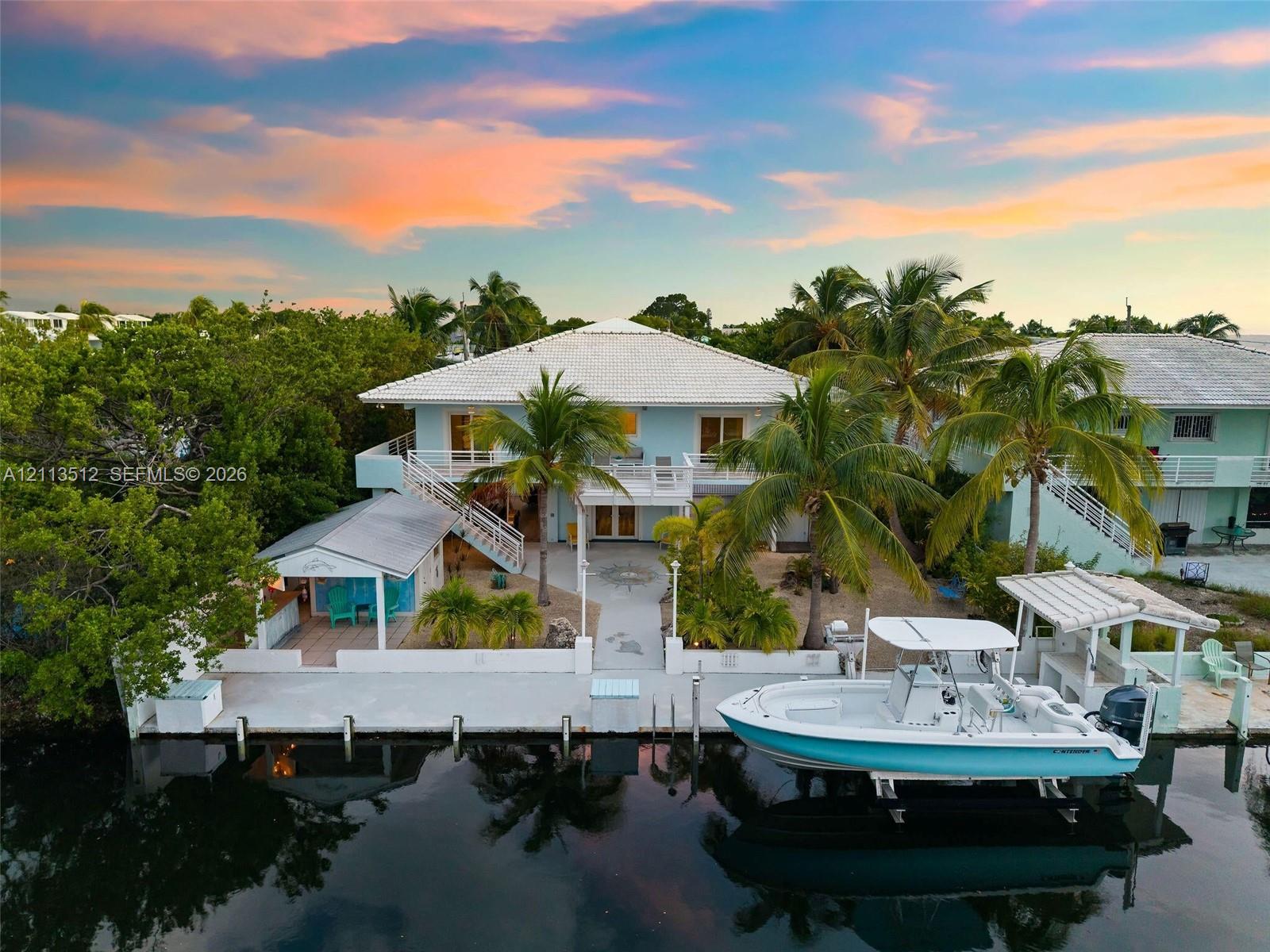 Waterfront residence featuring a private concrete dock, boat lift, expansive ground-level patio, and exterior staircase