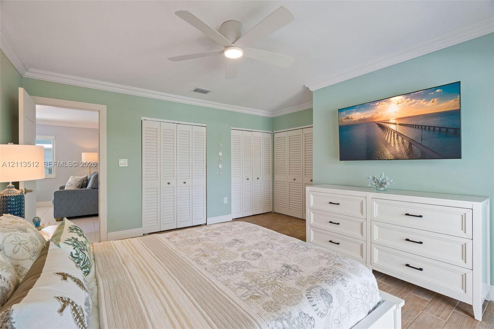 Neutral wall palette with crown molding, white louvered-style closet doors, and a ceiling-mounted light fixture with integrated fan blades