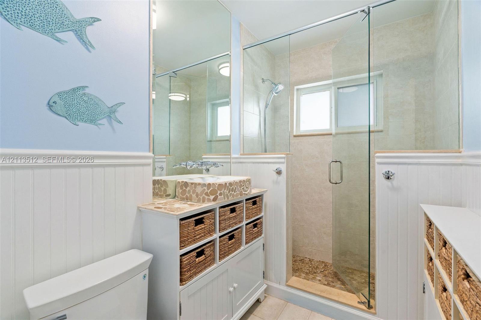 Bathroom featuring a vanity with a stone-accented vessel sink, beadboard wainscoting, glass-enclosed shower, and built-in storage cabinetry