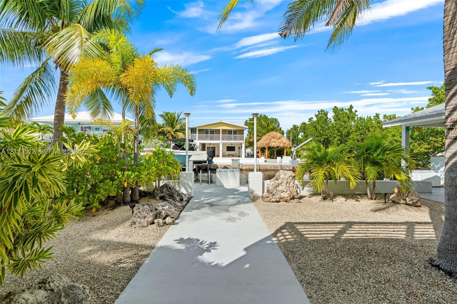 Waterfront property featuring a private boat slip, concrete walkway, gravel landscaping, and mature palm trees