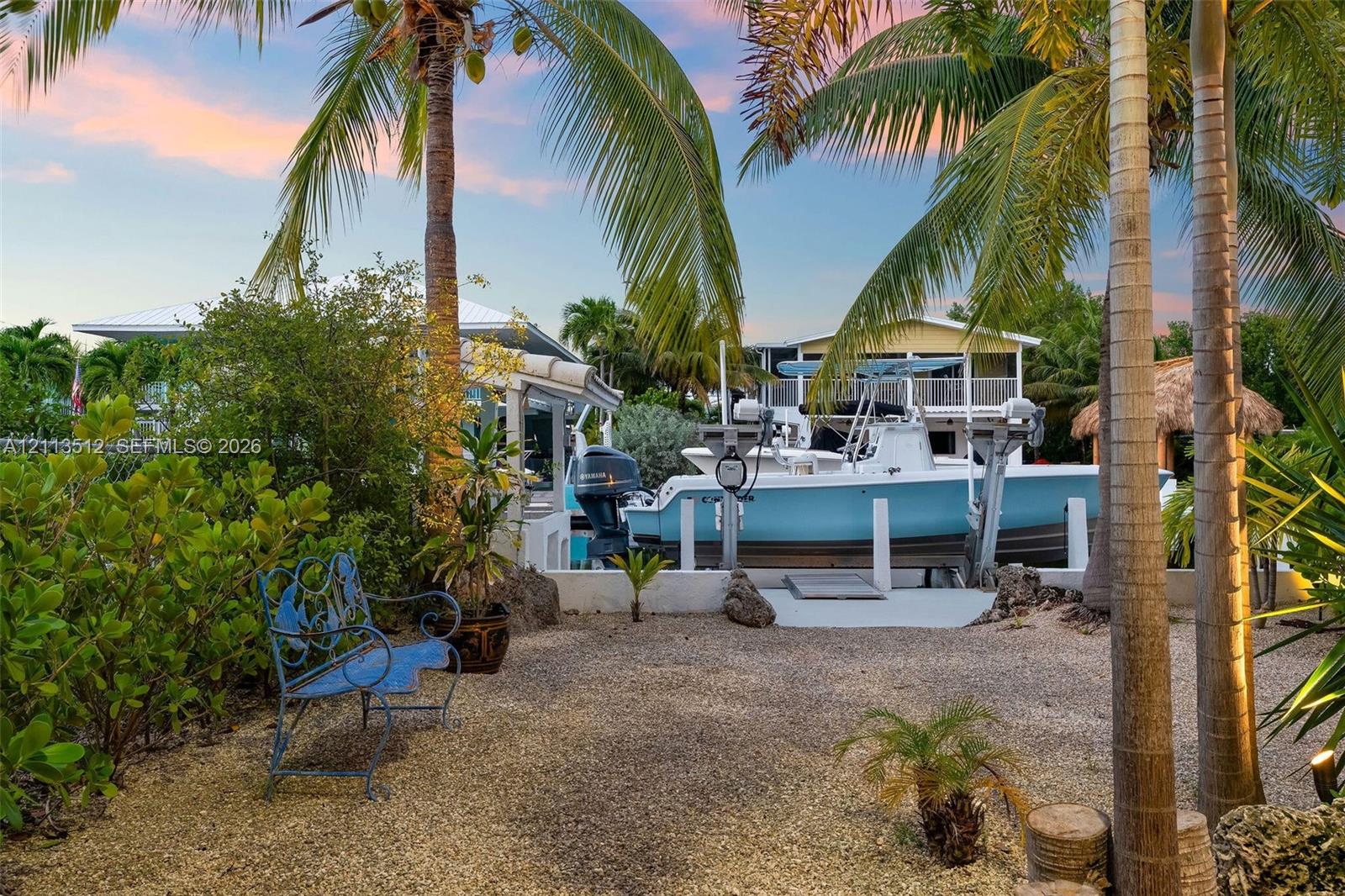 Waterfront property featuring a private boat lift, concrete dock, gravel ground cover, and mature palm trees