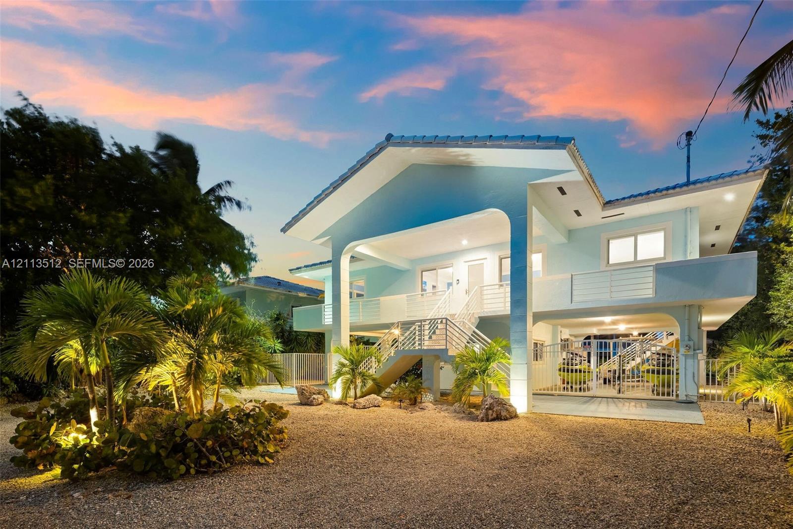 Elevated multi-story residence featuring a covered entryway, dual-level railed balconies, and a gravel ground-level exterior