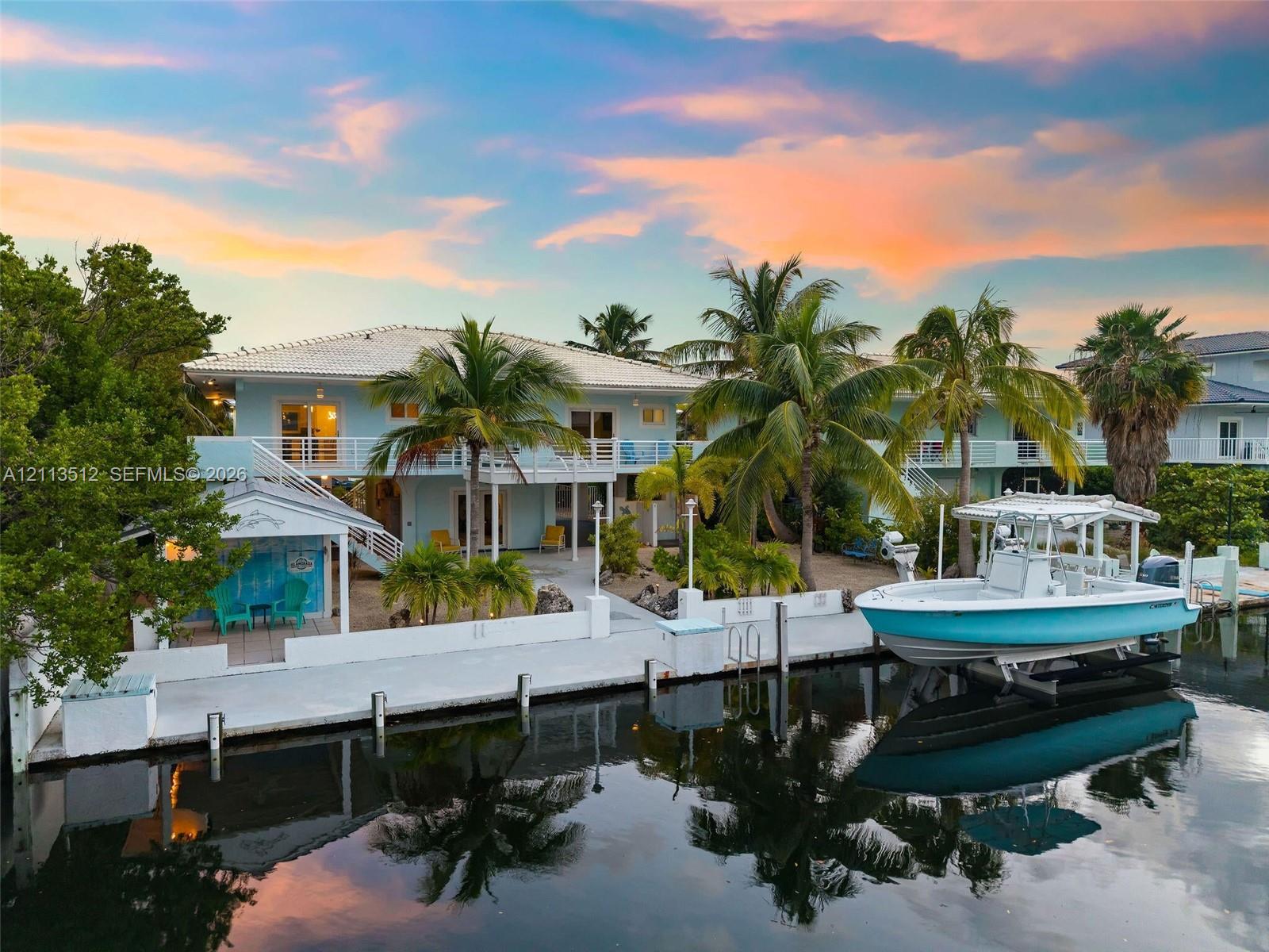Waterfront property featuring a private boat dock with lift, concrete seawall, covered patio space, and two-story exterior balcony
