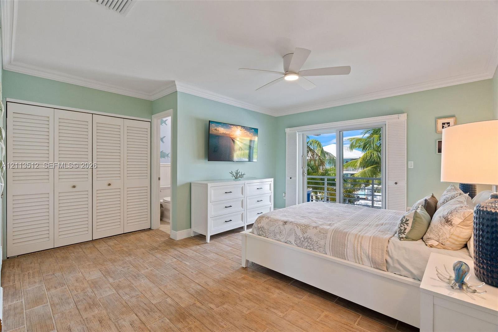 Wood-finish tile flooring, white louvered-door closets, crown molding, ceiling fan, and sliding glass doors with balcony access