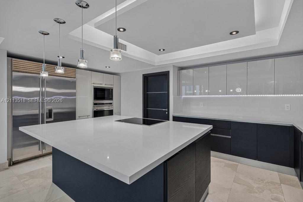Contemporary kitchen featuring a spacious center island with a stone countertop, high-gloss cabinetry, stainless steel professional-grade appliances, recessed ceiling lighting, and tile flooring