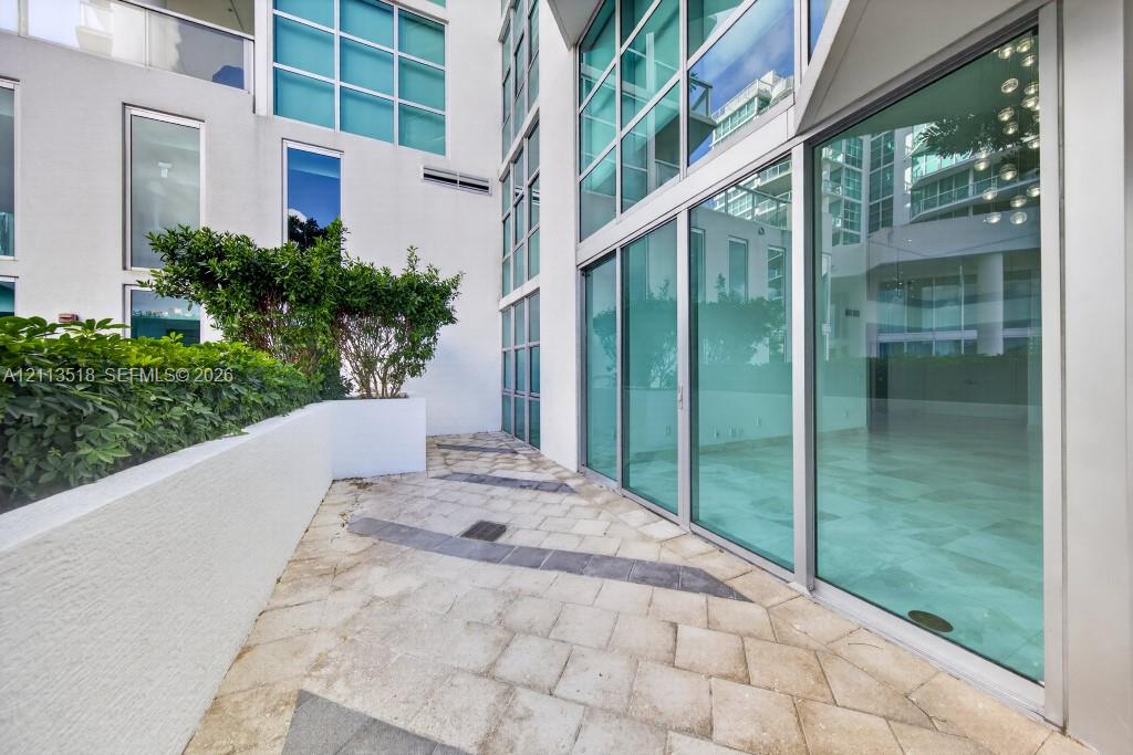 Private terrace featuring large-format stone pavers, integrated concrete planter beds with mature shrubbery, and floor-to-ceiling glass wall panels with metal frames