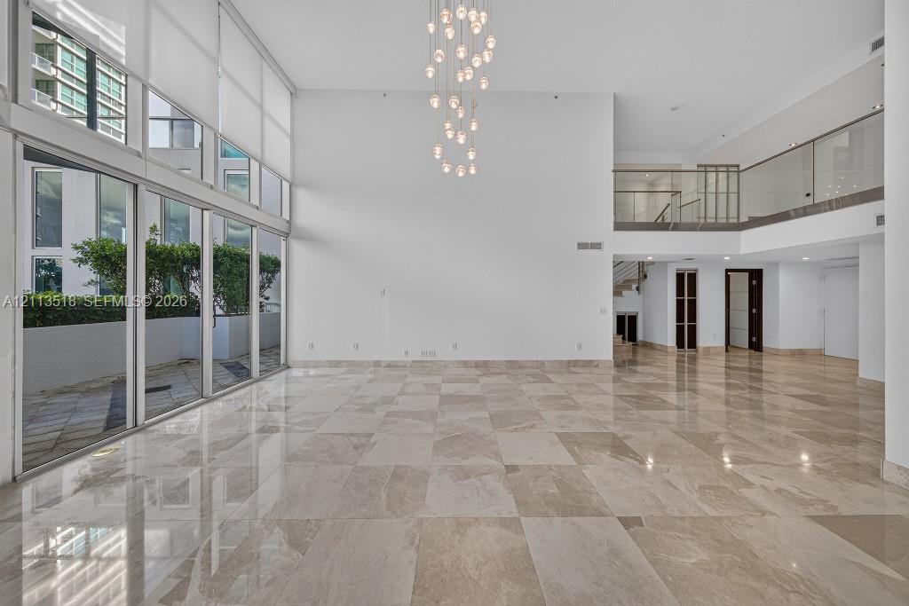 Expansive interior space featuring double-height ceilings, floor-to-ceiling windows, polished stone flooring, a multi-pendant light fixture, and a mezzanine level with glass railings