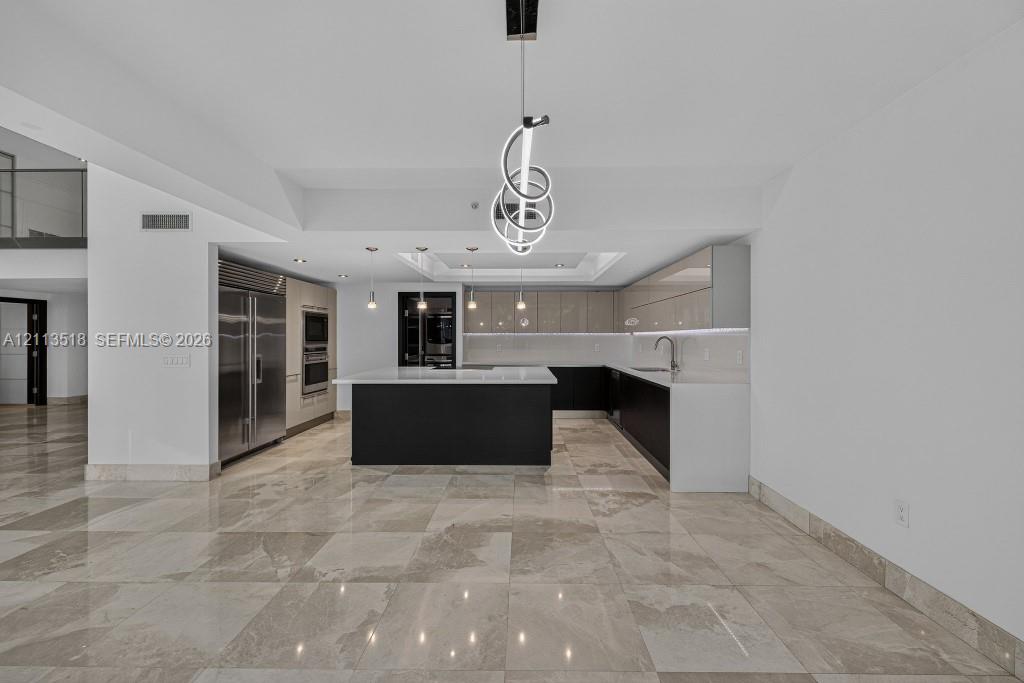 Kitchen featuring high-gloss cabinetry, stone countertops, central island, integrated stainless steel appliances, and large-format tile flooring