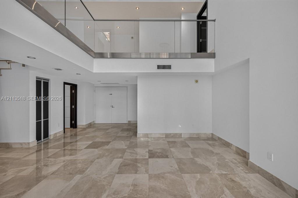 Interior space featuring high ceilings, polished stone flooring, a glass-panel mezzanine railing, recessed lighting, and multi-panel doors
