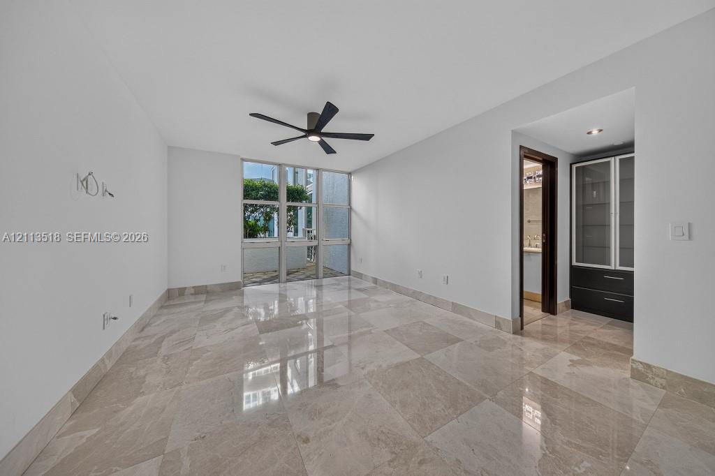 Interior space featuring large-format stone tile flooring, floor-to-ceiling windows, a ceiling fan with integrated lighting, and built-in cabinetry with glass-front uppers