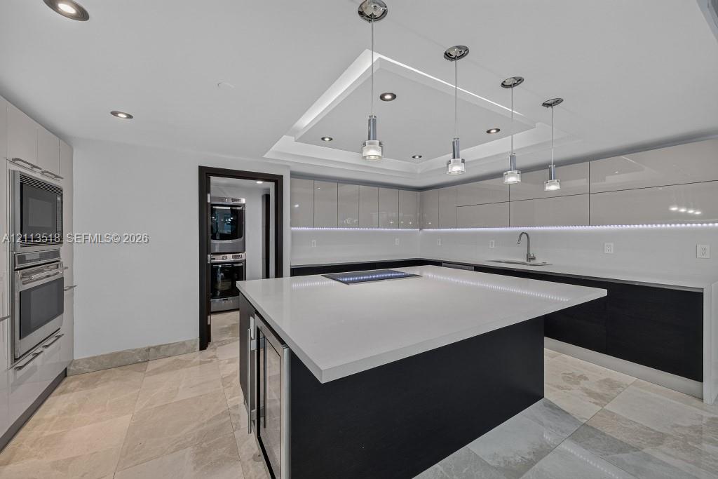 Kitchen featuring high-gloss cabinetry, a central island with a solid-surface countertop, recessed tray ceiling lighting, stainless steel built-in appliances, and tile flooring