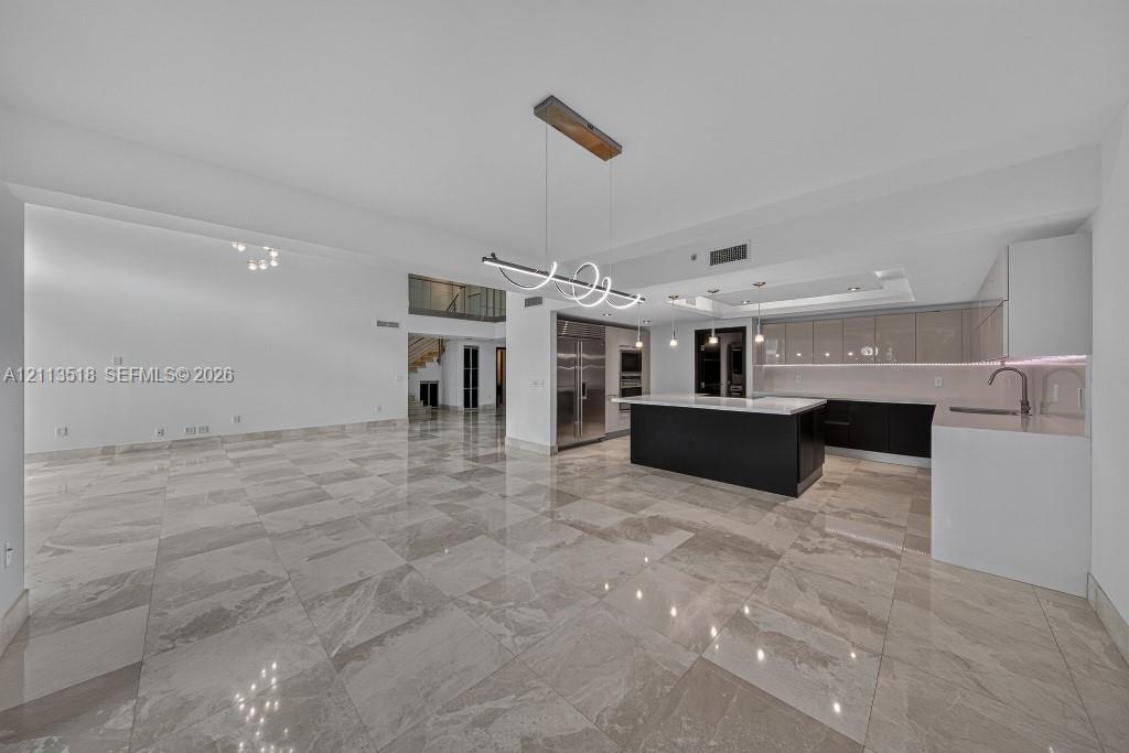 Open-concept interior featuring large-format tile flooring, a kitchen island with a neutral countertop, stainless steel built-in appliances, flat-panel cabinetry, and contemporary geometric pendant lighting
