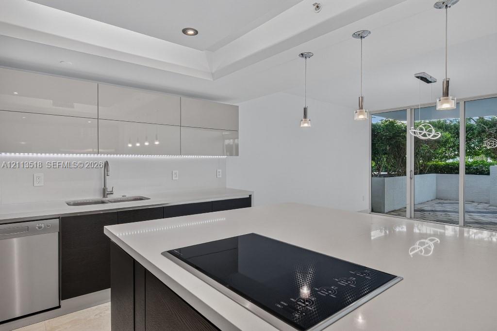 Kitchen featuring high-gloss cabinetry, stone countertops, a stainless steel dishwasher, a built-in cooktop, and recessed tray ceiling lighting
