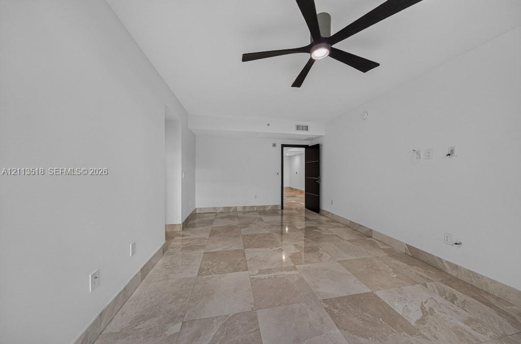 Spacious room featuring polished large-format stone tile flooring, neutral wall finishes, and a contemporary matte black ceiling fan with integrated lighting