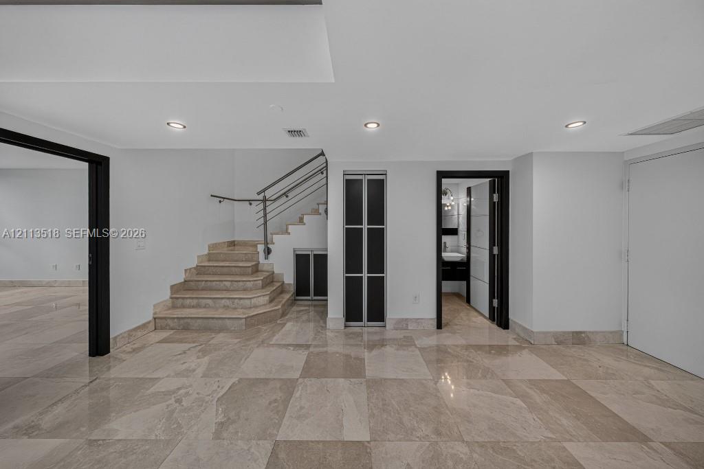 Polished stone flooring, recessed lighting, staircase with metal railings, and contrasting dark-framed doorways