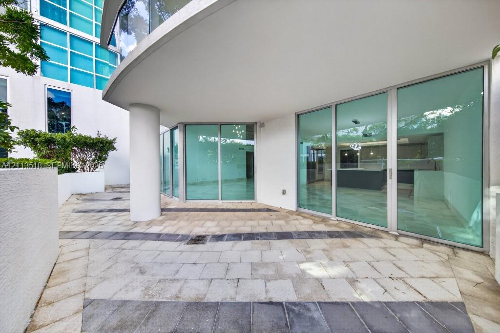 Curved stone patio featuring decorative inlaid tile patterns, expansive floor-to-ceiling glass walls, and a structural concrete support column