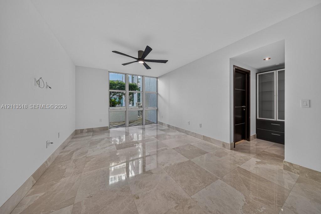 Polished stone flooring, floor-to-ceiling windows, dark wood-finish interior doors, recessed ceiling lighting, and built-in cabinetry with glass-front shelving