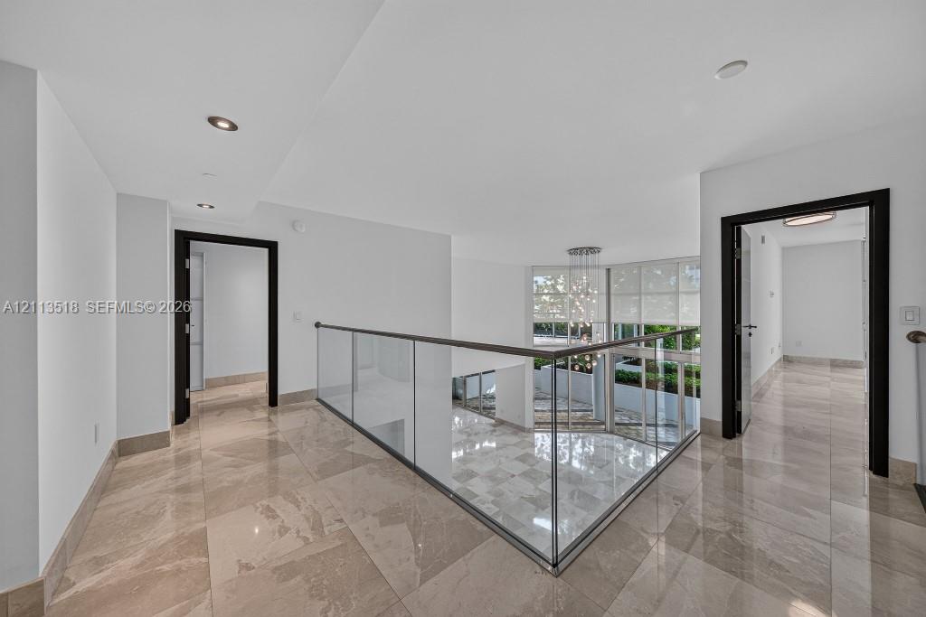 Polished tile flooring, glass panel railing with a metal handrail, recessed lighting, and dark-toned door frames