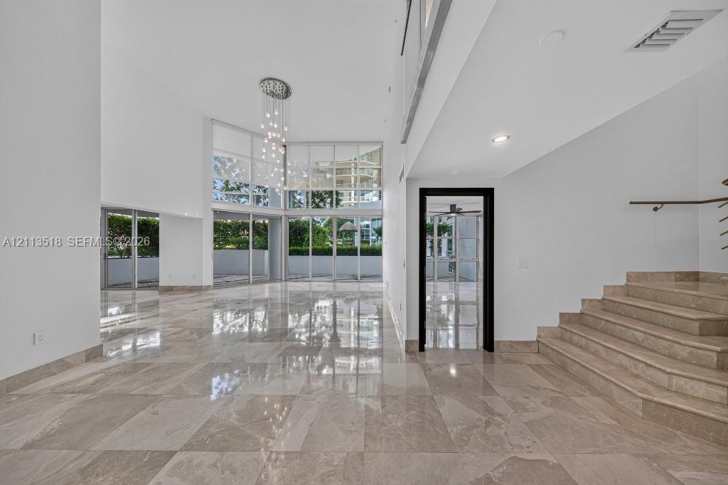 Double-height ceilings, floor-to-ceiling glass wall, polished stone flooring, custom multi-light chandelier, and stone staircase Double-height ceilings, floor-to-ceiling glass wall, polished stone flooring, custom multi-light chandelier, and stone staircase