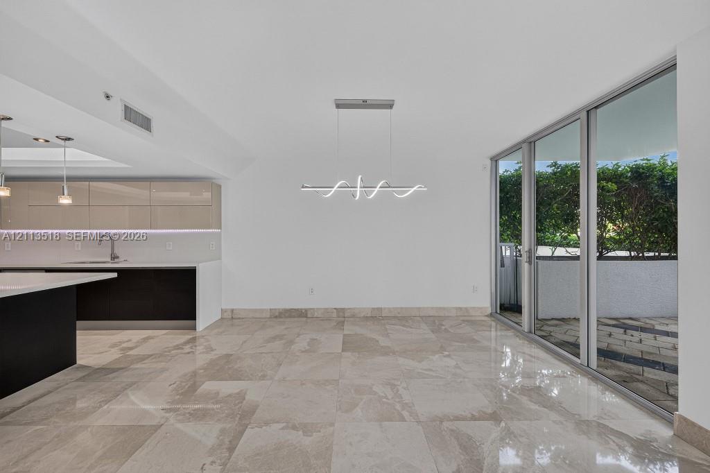 Open-concept interior featuring large-format tile flooring, high-gloss cabinetry, a quartz waterfall island, modern linear architectural lighting, and floor-to-ceiling glass sliding doors Open-concept interior featuring large-format tile flooring, high-gloss cabinetry, a quartz waterfall island, modern linear architectural lighting, and floor-to-ceiling glass sliding doors