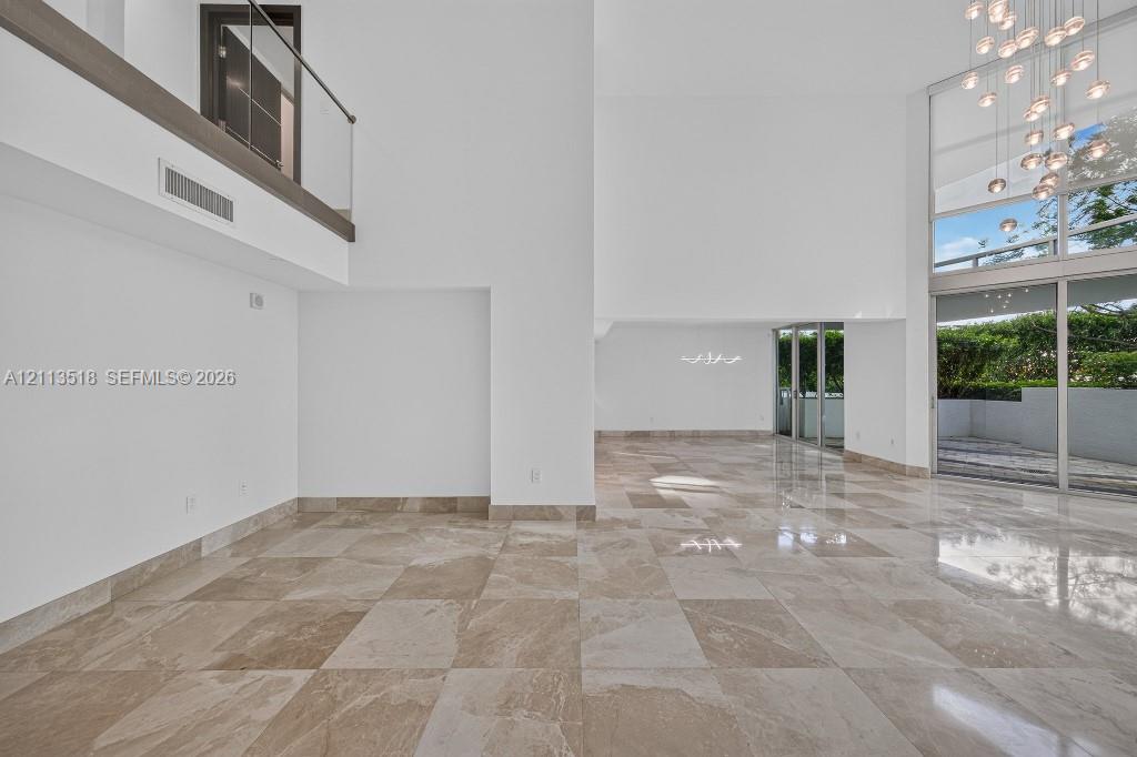 Double-height ceilings featuring floor-to-ceiling windows, polished stone flooring, a multi-pendant chandelier, and a glass-paneled mezzanine railing Double-height ceilings featuring floor-to-ceiling windows, polished stone flooring, a multi-pendant chandelier, and a glass-paneled mezzanine railing