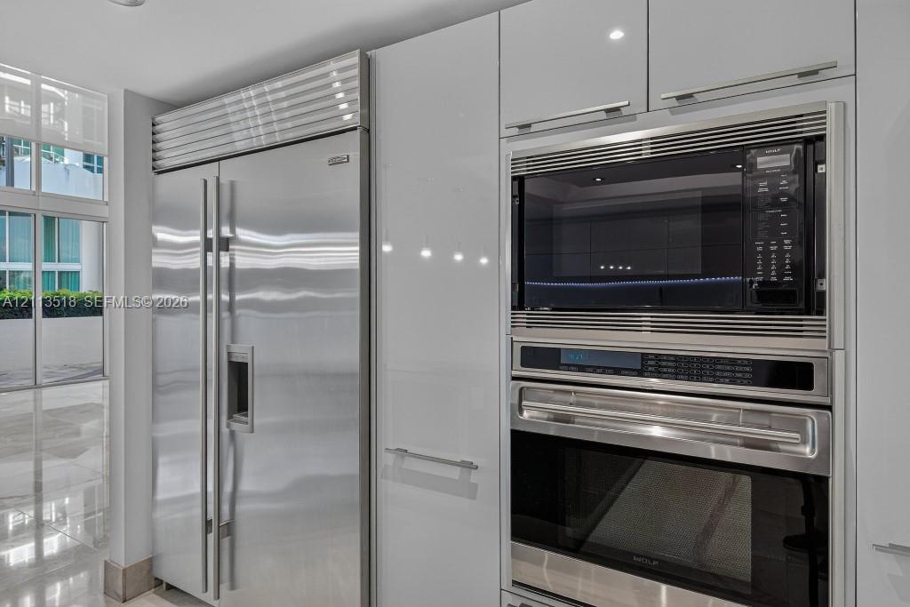 Gloss-finish cabinetry with stainless steel hardware, integrated side-by-side refrigerator, built-in microwave, and wall oven