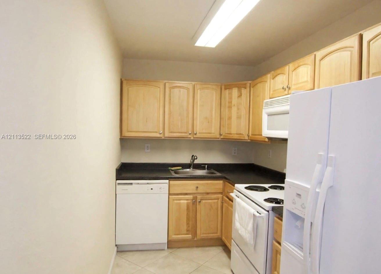 Kitchen featuring light-finish cabinetry, solid surface countertops, a stainless steel sink with a high-arch faucet, and white appliances Kitchen featuring light-finish cabinetry, solid surface countertops, a stainless steel sink with a high-arch faucet, and white appliances
