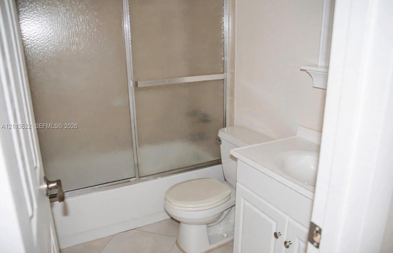 Bathroom featuring white cabinetry, integrated sink, tub-shower combination with sliding glass doors, and light-toned tile flooring Bathroom featuring white cabinetry, integrated sink, tub-shower combination with sliding glass doors, and light-toned tile flooring